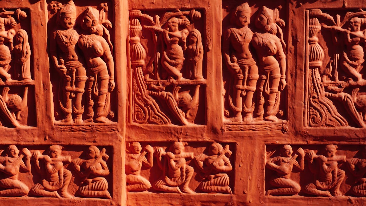 Detailed stone carvings depicting historical and cultural figures from ancient times at a temple wall.